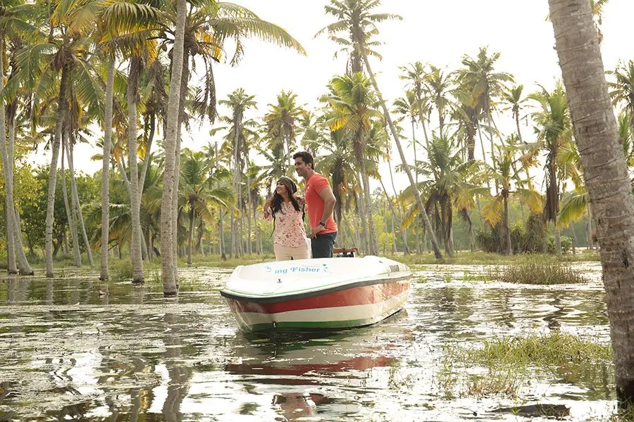 Couple beside a speed boat in a coconut grove on the Poovar backwaters